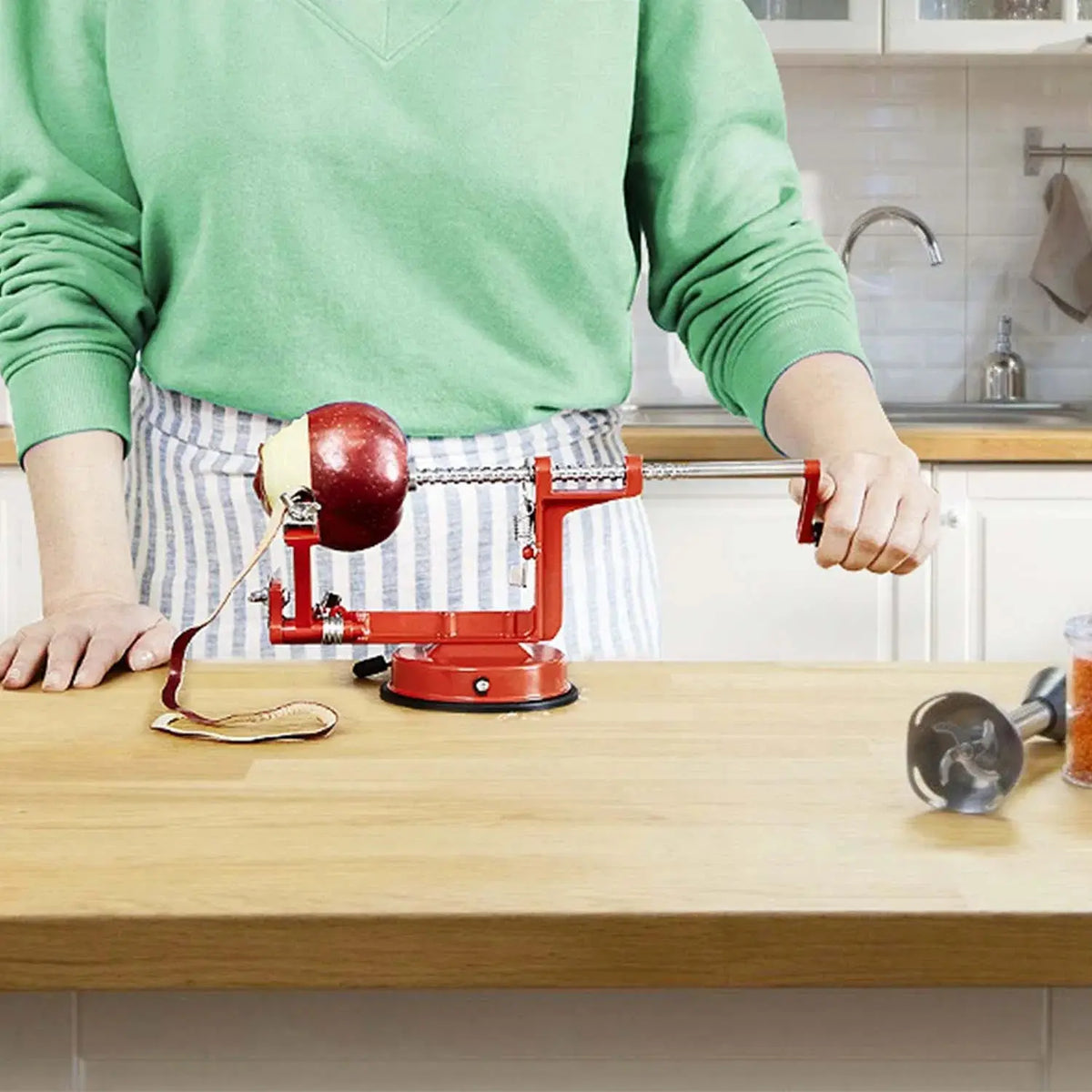OrchardSpin apple peeler clamped to a kitchen counter, peeling a red apple with the hand crank